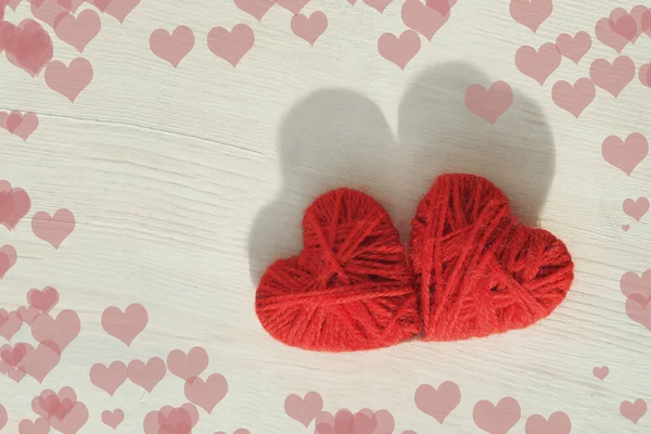 Dos corazones rojos hechos a mano de hilos de lana sobre un fondo claro de madera — Foto de Stock