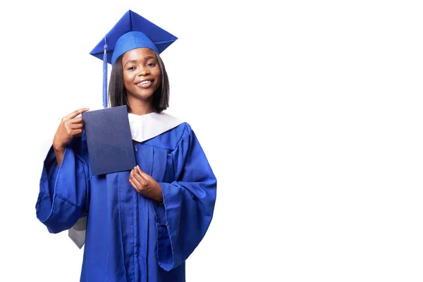 Mujer negra con una bata azul sobre un fondo blanco sonríe y muestra diploma Imágenes de stock libres de derechos