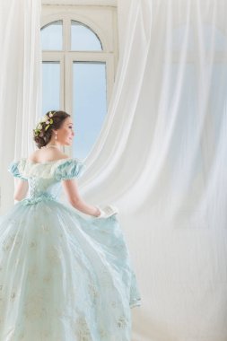 Arka planda pencereli, tarihi elbiseli, zarif, siyah saçlı kadın.