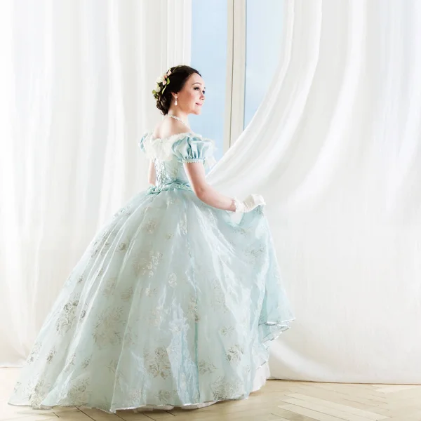 Hermosa mujer de pelo oscuro elegante en vestido histórico en el fondo con ventana —  Fotos de Stock