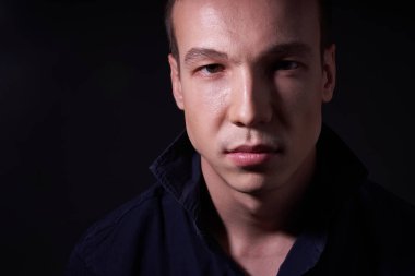 Kendine güveni olan güzel bir gencin fotokopi stüdyosundaki siyah izole bir arka planda çekilmiş portresini yakından çeker ve kameraya bakar.