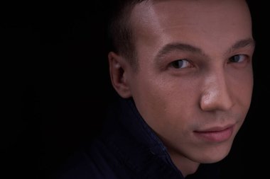 Kendine güveni olan güzel bir gencin fotokopi stüdyosundaki siyah izole bir arka planda çekilmiş portresini yakından çeker ve kameraya bakar.