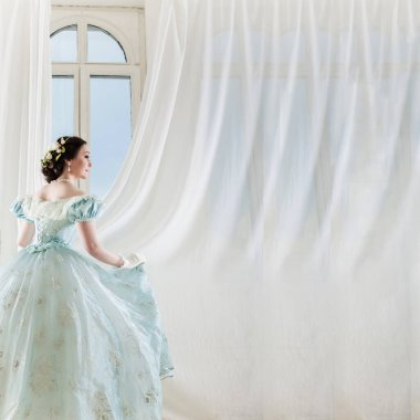 Arka planda pencereli, tarihi elbiseli, zarif, siyah saçlı kadın.