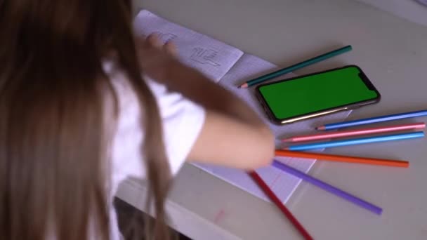 Little girl studies, does lessons, uses a phone with a green screen — Stock Video