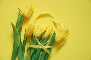 Sarı bir zemin üzerinde beş sarı lale ve kurdeleden yapılmış bir kalp..