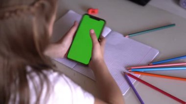 Küçük bir kız elinde telefonla masada oturuyor, Chroma 'ya bakıyor.