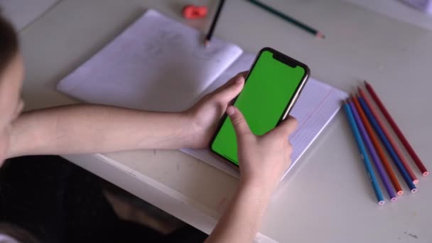 Een klein meisje zit aan een tafel met telefoon in handen, ze kijkt naar de Chroma — Stockvideo