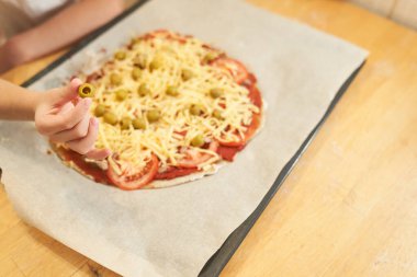 Arka planda pizza ve zeytin olan bir çocuk eli..