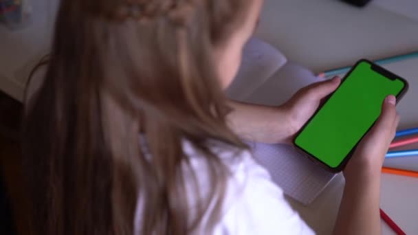 Een klein meisje zit aan een tafel met telefoon in handen, ze kijkt naar de Chroma — Stockvideo