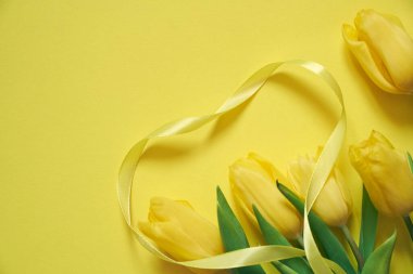 Sarı bir zemin üzerinde beş sarı lale ve kurdeleden yapılmış bir kalp..