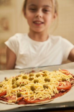 Kız, biftekli pizza pişirmek için hazırlanmış bir yemek tepsisini tutuyor. Yemek pişirme.