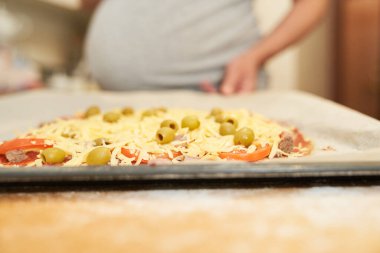 Hamile kadın, elinde pizza pişirmek için hazırlanmış bir çarşaf tutuyor. Evde yemek yapıyor.