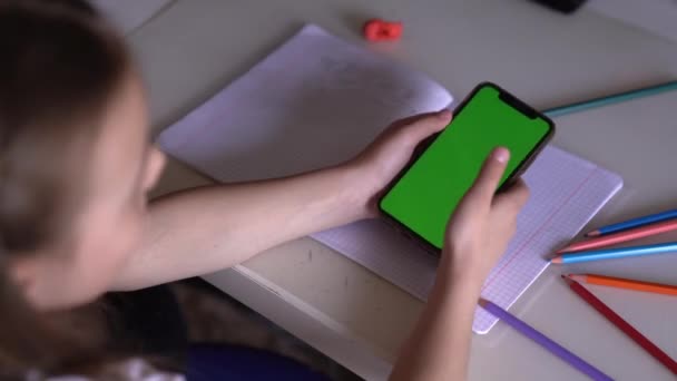 A little girl plays on her phone instead of school home work. — Stock Video