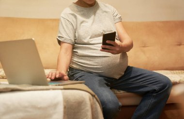 Evde telefonlu hamile bir kadın bilgisayar başında internetten alışveriş yapıyor.