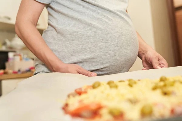 Schwangere hält sich an ein Backblech, das zum Pizzabacken vorbereitet ist.Kochen zu Hause — Stockfoto