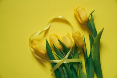 Sarı bir zemin üzerinde beş sarı lale ve kurdeleden yapılmış bir kalp..