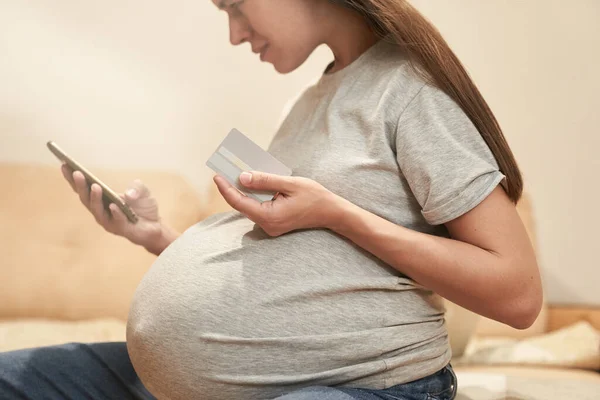 Schwangere Frau zu Hause mit Telefon sitzt mit Kreditwagen, Online-Shopping — Stockfoto