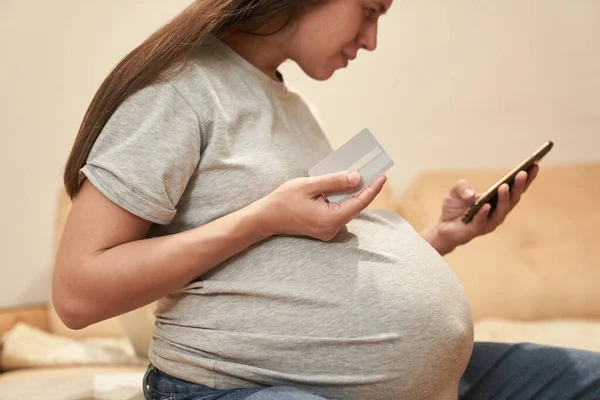 Schwangere Frau zu Hause mit Telefon sitzt mit Kreditwagen, Online-Shopping — Stockfoto