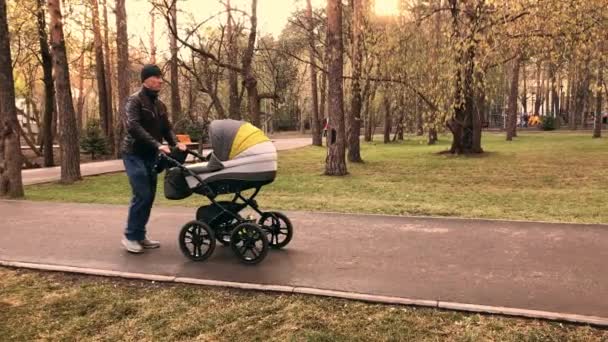 Slow-motion video of father walking with newborn baby in stroller in the evening — Stock Video