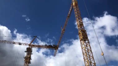 Mavi gökyüzünde iki sarı vinç, güzel bulutlar, inşaat işleri.