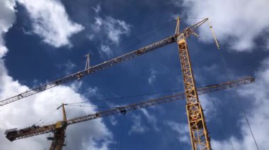 Mavi gökyüzünde iki sarı vinç, güzel bulutlar, inşaat işleri.