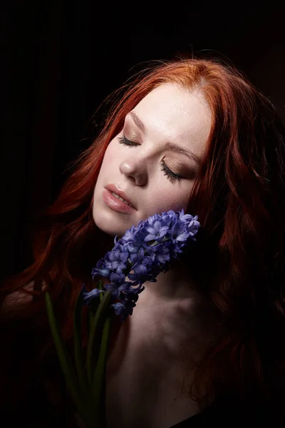 Portrait of girl with long red hair, good skin, with hyacinth on a black background — Stock Photo, Image