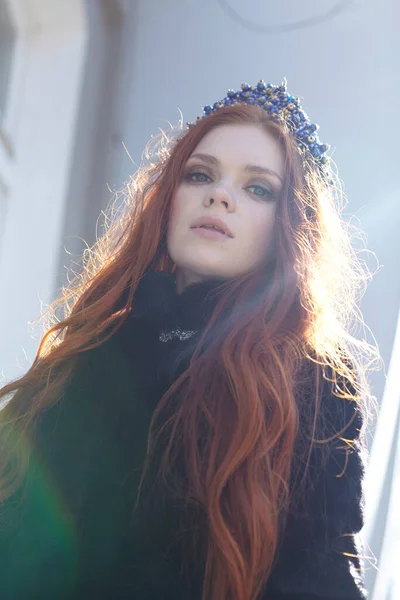 Beautiful red head girl with long hair in a crown of pearls stands on the street — Stock Photo, Image