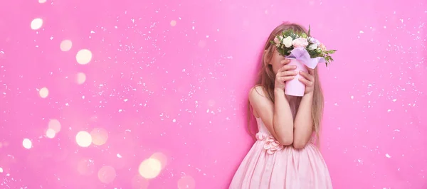 Malá holčička v růžových šatech s kyticí květin, schovaná za květinami. — Stock fotografie