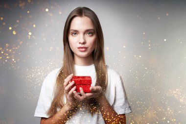 Gülümseyen güzel bir genç kadın içinde mücevher olan kapalı bir hediye kutusu tutuyor. Tatil konsepti, hediyeler