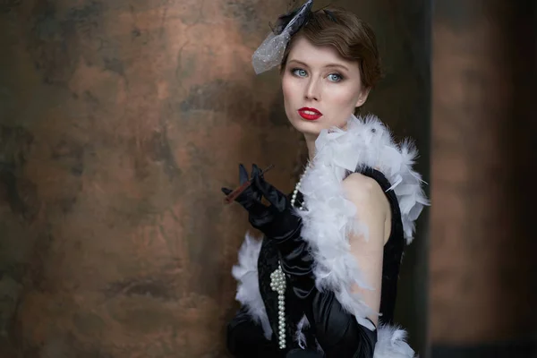 A young beautiful woman in a historical costume of the 20s or 30s of the XX century with a boa and a mouthpiece — Stock Photo, Image