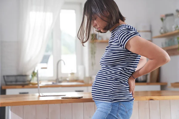 Eine junge schwangere Frau hält ihr mit den Händen den Rücken frei. Eine Brünette im dritten Schwangerschaftsdrittel. Das Konzept der Rückenschmerzen während der Schwangerschaft. — Stockfoto