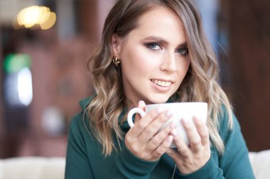 Güzel bir manikürlü, elinde fincanla bir kafede oturan güzel bir kadının yakın plan portresi. Kız doğrudan kameraya bakıyor.