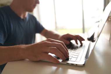 Bir adamın eli dizüstü bilgisayarın klavyesinde, klavyede yazarken yakın plan. Uzaktan çalışma konsepti bir projede çalışmak, metni girmek, bir şeyleri düzenlemek. Uzaktan çalışma konsepti, ev ofisi.