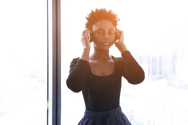 An African-American woman listens to music with headphones. A young woman in a sports uniform on the background of a window