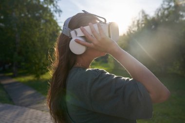 Elleriyle sanal gerçeklik gözlüğü takan kız yeşil ağaçların arka planında duruyor. Gelecek kavramı..