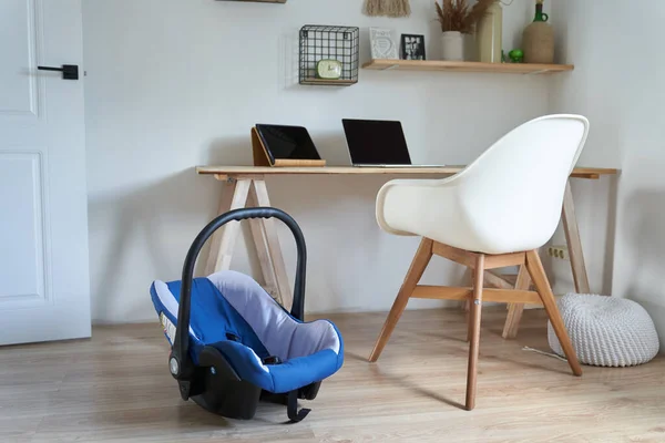 Snygg inredning i arbetsområdet med ett designat vitt bord, stol, laptop och surfplatta på bordet. Det finns en bilbarnstol bredvid. Begreppet modern inredning. — Stockfoto