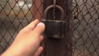 El, demir tel örgüye asma kilit takar. Kilidin kapalı olup olmadığını kontrol eder.