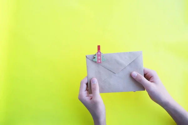 In the hands of a paper envelope with a herringbone on a yellow background, close-up. Letter to santa claus.