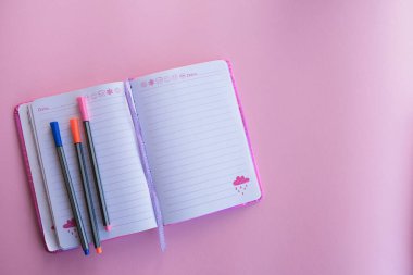 Not defterleri, renkli kalemler ve gözlüklerle düz kompozisyon, pembe arkaplan.