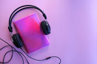 Mor bir arka planda, kırmızı bir not defteri ve kulaklıklar, düz yatıyordu..