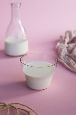 Pembe arka planda taze sütle cam bardak ve şişe..