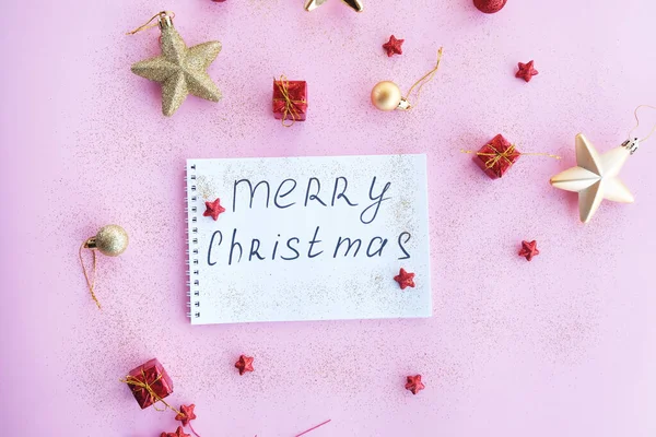 Holiday decorations and a notebook with the inscription: Merry Christmas, onwhite notepad, flat style. Pink background.Christmas planning concept.