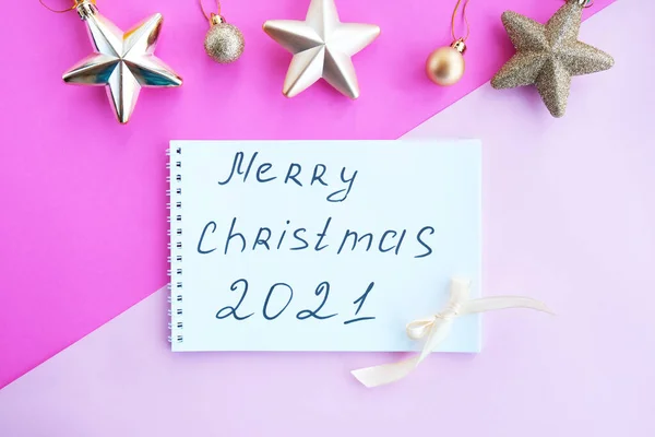 Holiday decorations and a notebook with the inscription: Merry Christmas, onwhite notepad, flat style. Pink background.Christmas planning concept.