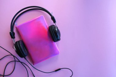 Mor bir arka planda, kırmızı bir not defteri ve kulaklıklar, düz yatıyordu..