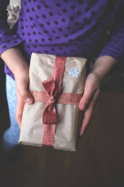 Руки держат подарок завернутый в бумагу и красную ленту в помещении. — стоковое фото