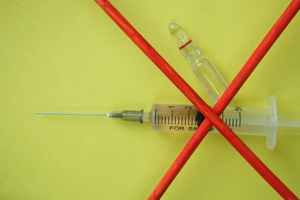 Syringe with vaccine covered with a red cross on a yellow background. COVID-19. — Stock Photo, Image