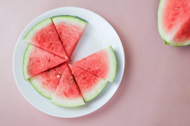 Pembe arka planda yuvarlak bir tabakta karpuz parçaları. Üst manzara, düz kat. Olgun karpuz dilimleri. Vejetaryen yemekleri.