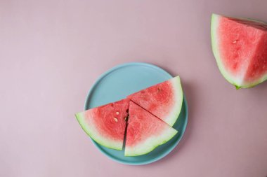 Pembe arka planda yuvarlak bir tabakta karpuz parçaları. Üst manzara, düz kat. Olgun karpuz dilimleri. Vejetaryen yemekleri.