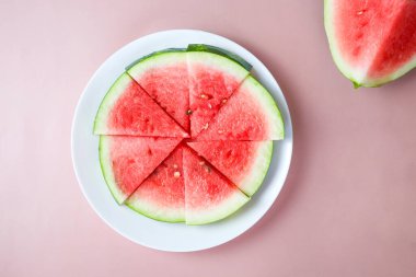 Pembe arka planda büyük kırmızı çiğ karpuz dilimleri, uzay manzarasını kopyala. Et tatlıdır, suludur, genellikle koyu kırmızıdan pembeye.