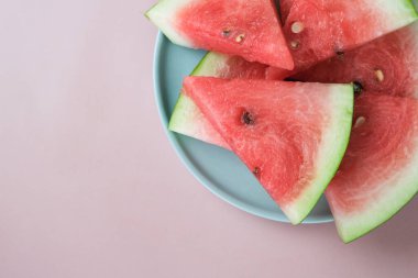 Pembe arka planda büyük kırmızı çiğ karpuz dilimleri. Et tatlıdır, suludur, genellikle koyu kırmızıdan pembeye.